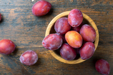 Ripe plums in a wooden bowl on the table.