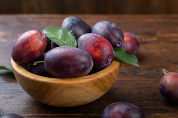 Fresh plums with leaves in a wooden bowl on a brown table.