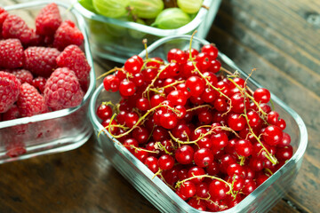 Assorted berries of raspberries, gooseberries and red currants in glass bowls on a wooden table.