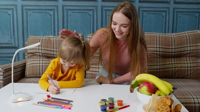 Lovely mother babysitter teacher helping kid daughter with homework, learning writing at home