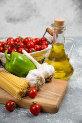 Cherry tomatoes, pastas, garlic, green pepper and olive oil on a wooden board