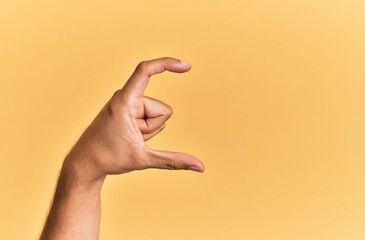 Arm and hand of caucasian man over yellow isolated background picking and taking invisible thing, holding object with fingers showing space