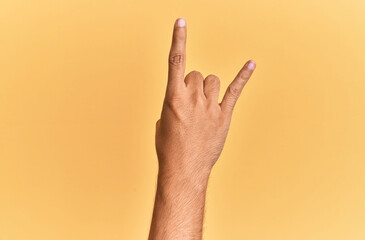 Arm and hand of caucasian man over yellow isolated background gesturing rock and roll symbol, showing obscene horns gesture