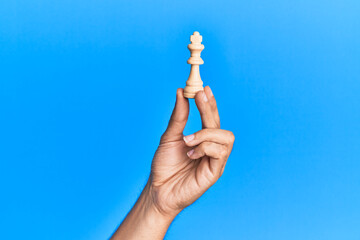 Hand of hispanic man holding king chess piece over isolated blue background.