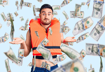 Young handsome man wearing lifejacket clueless and confused expression with arms and hands raised....