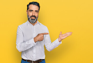 Middle aged man with beard wearing casual white shirt amazed and smiling to the camera while presenting with hand and pointing with finger.