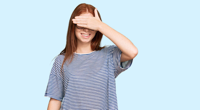 Young read head woman wearing casual clothes and glasses smiling and laughing with hand on face covering eyes for surprise. blind concept.