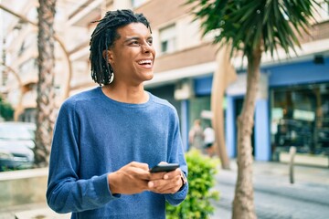 Young african american man smiling happy using smartphone at street of city.