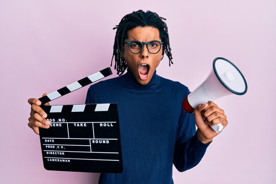 Young African American Man Holding Video Film Clapboard And Megaphone In Shock Face, Looking Skeptical And Sarcastic, Surprised With Open Mouth