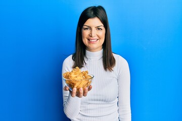 Young hispanic woman holding uncooked pasta bowl looking positive and happy standing and smiling with a confident smile showing teeth