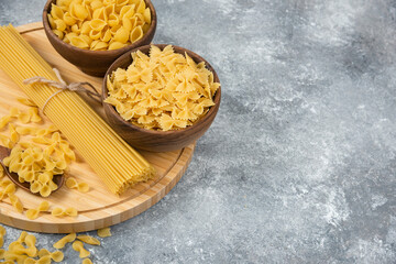 Bowls of raw dry pasta and spaghetti on marble surface