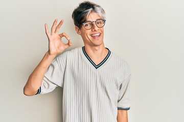 Young hispanic man wearing casual clothes and glasses smiling positive doing ok sign with hand and...