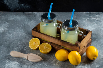 Two glass jars of lemon juice with straws and slices on a wooden basket