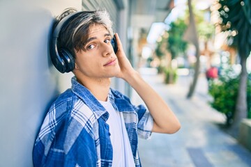 Young hispanic man with serious expression using headphones at the city.