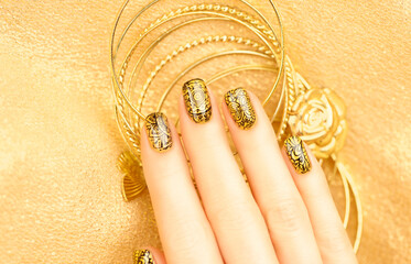 Female fingers with mehendi style manicure. Beautiful golden manicure on a golden background.