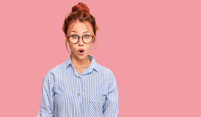 Young redhead woman wearing casual clothes and glasses scared and amazed with open mouth for...