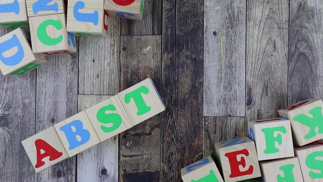 Colourful alphabet letters on wooden cubes with word - abstract - in a diagonal line with additional blocks decorating the corners of the frame. Stop motion, top view