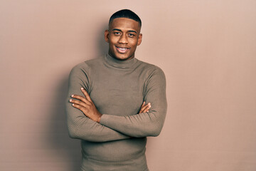 Young black man wearing casual turtleneck sweater happy face smiling with crossed arms looking at...