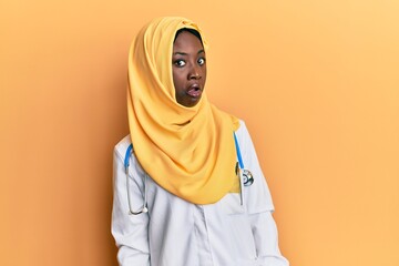 Beautiful african young woman wearing doctor uniform and hijab in shock face, looking skeptical and sarcastic, surprised with open mouth