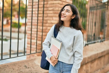 Young middle east student girl smiling happy holding book at the city.