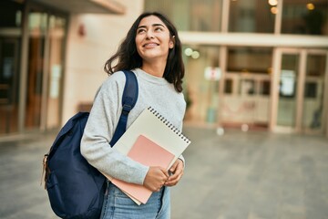 Young middle east student girl smiling happy holding book at the city.
