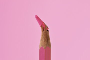 Close-up of broken tip of pink colored pencil on pink background - Concept of violence against women