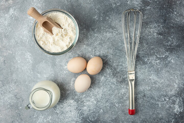 Bowl of flour, eggs and whisker on marble surface