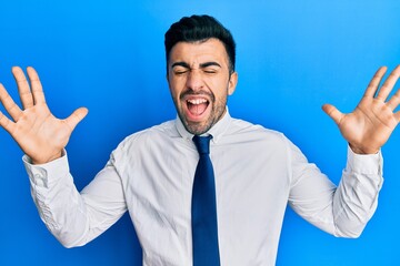 Young hispanic man wearing business clothes celebrating mad and crazy for success with arms raised and closed eyes screaming excited. winner concept