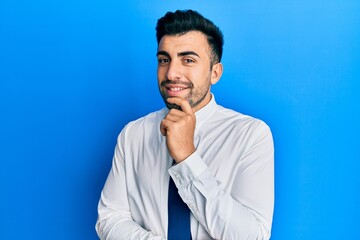 Young hispanic man wearing business clothes looking confident at the camera with smile with crossed arms and hand raised on chin. thinking positive.