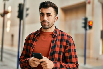 Young hispanic man with serious expression using smartphone at the city.