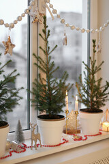 Small potted fir trees and Christmas decor on window sill indoors