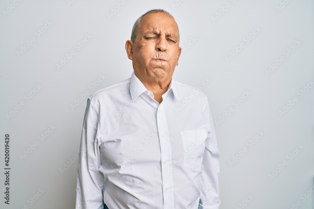 Poster Handsome senior man wearing casual white shirt puffing cheeks with funny face. mouth inflated with air, crazy expression.