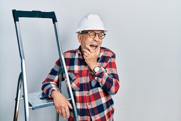 Handsome mature handyman close to construction stairs wearing hardhat laughing and embarrassed...