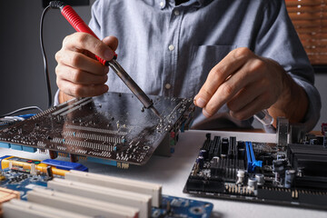 Technician repairing electronic circuit board with soldering iron at table, closeup