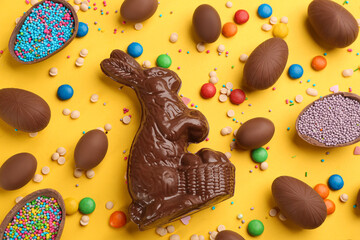 Flat lay composition with chocolate Easter bunny, eggs and candies on yellow background