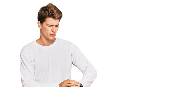 Handsome caucasian man wearing casual white sweater checking the time on wrist watch, relaxed and confident