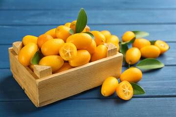 Fresh ripe kumquats in crate on blue wooden table