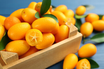 Fresh ripe kumquats in crate on blue wooden table, closeup