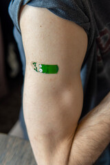 A man's arm with a fun, colorful, adhesive bandage after injection of vaccine or a scratch on the skin. First aid. Medical, pharmacy, and healthcare concept. After vaccination treatment.	