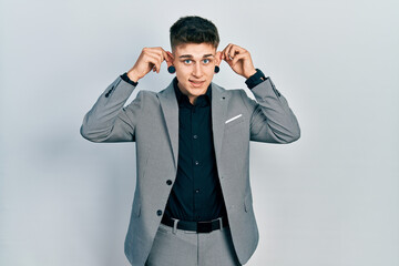Young caucasian boy with ears dilation wearing business jacket smiling pulling ears with fingers,...