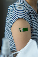 Arm of a woman with a colorful adhesive bandage after injection of vaccine or a scratch on the skin. First aid medical and healthcare concept. After vaccination treatment with mask and hand sanitizer.