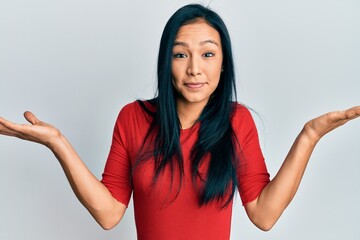 Beautiful hispanic woman wearing casual clothes clueless and confused with open arms, no idea and...
