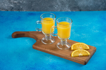 Two glass cups of tasty orange juice on a wooden board