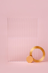 Ribbed acrylic plate and  golden ring on pastel pink background. Stylish background for presentation.