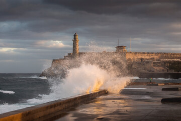 Fototapeta na wymiar Big waves on Malecon streets during sunrise with storm clouds in background. Havana, Cuba