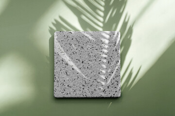 Square stone plate on green background with tropical leaf shadow. Stylish background for presentation.