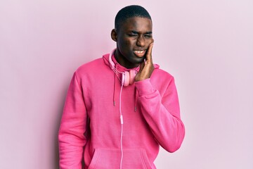 Young african american man wearing gym clothes and using headphones touching mouth with hand with painful expression because of toothache or dental illness on teeth. dentist