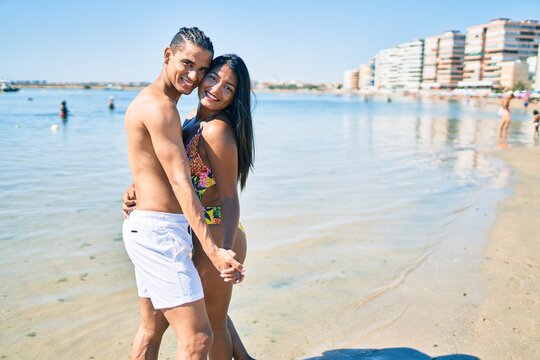 Young Latin Couple Wearing Swimwear  Smiling Happy And Dancing At The Beach.