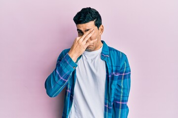 Fototapeta premium Handsome hispanic man wearing casual clothes smelling something stinky and disgusting, intolerable smell, holding breath with fingers on nose. bad smell