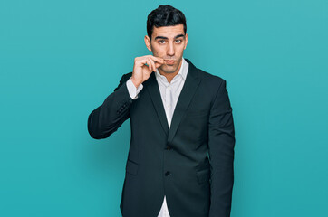 Handsome hispanic man wearing business clothes mouth and lips shut as zip with fingers. secret and...
